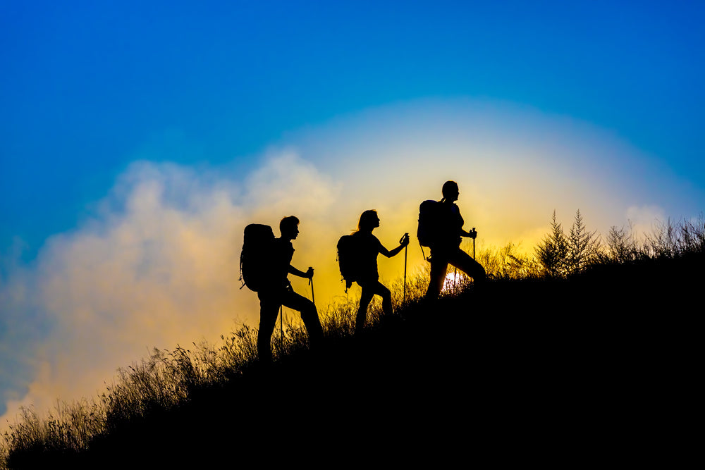 3 people walking up a hill in walking boots and with walking equipment